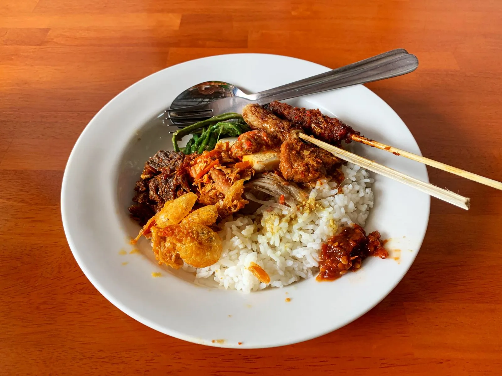 A plate of nasi campur on a plain wooden table