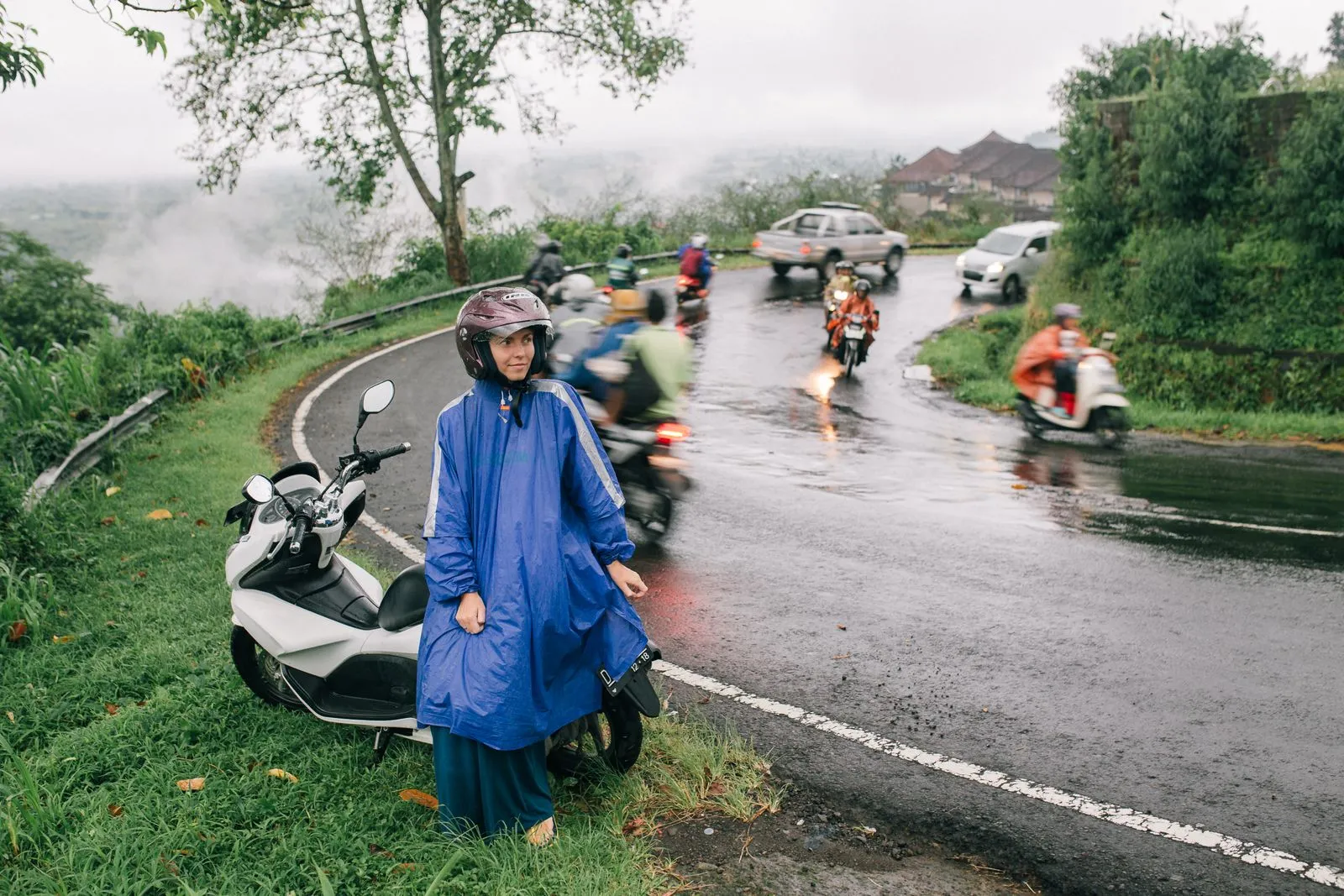 A wet mountain road in Bali with a scooter rider in a rain poncho
