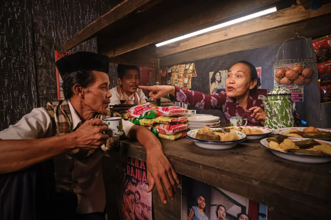Three people talking across the counter of a warung